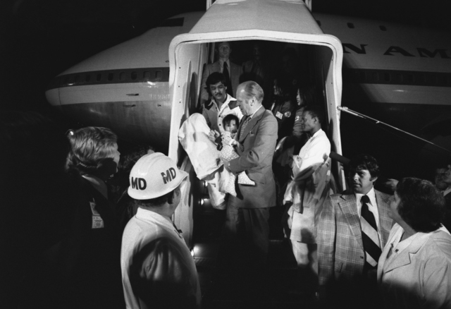 President Gerald R. Ford is depicted carrying a Vietnamese baby, likely an orphan, disembarking from a Clipper aircraft during Operation Babylift.